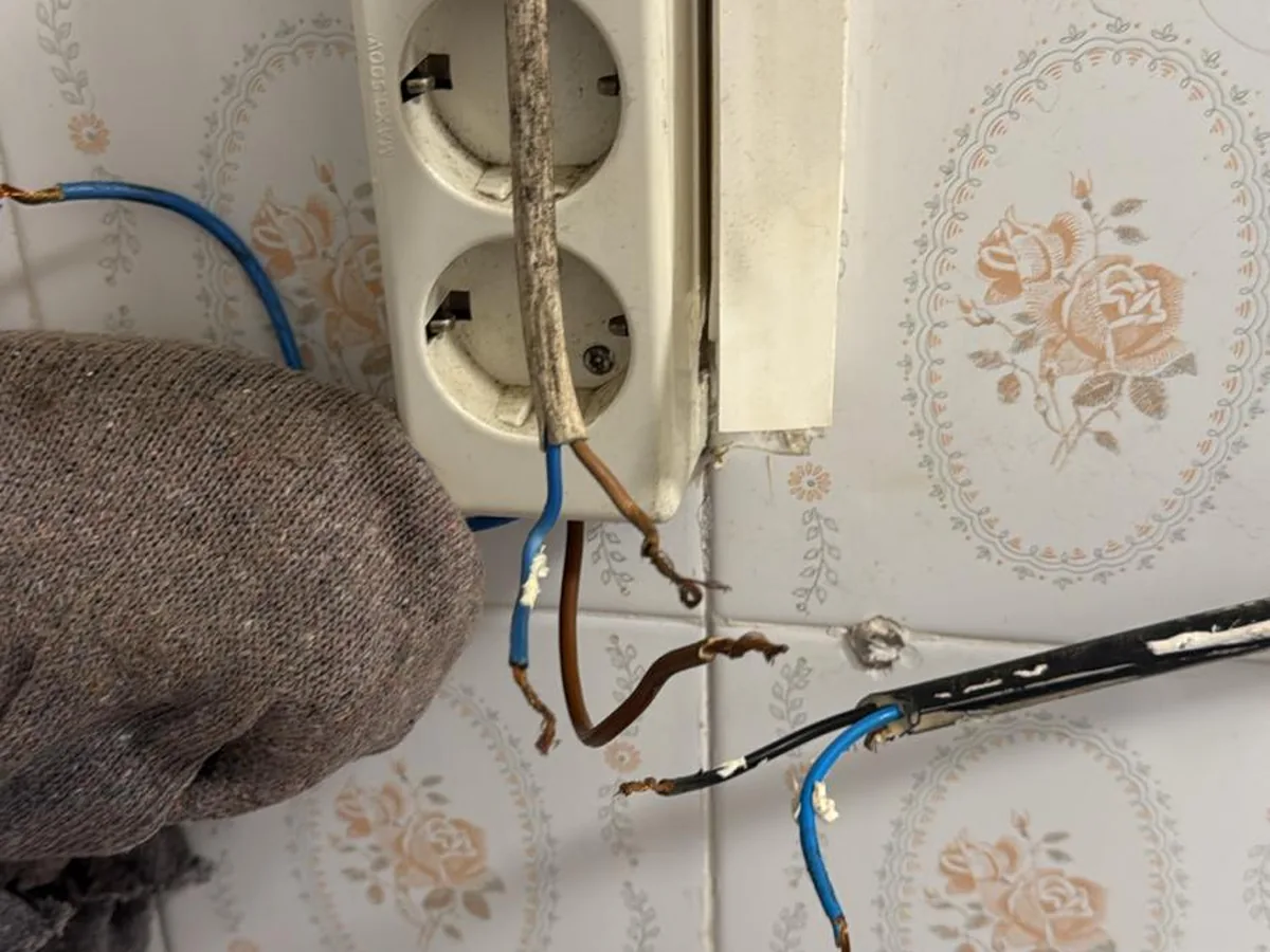Enchufe de superficie antiguo sobre azulejo con el cableado original a la vista